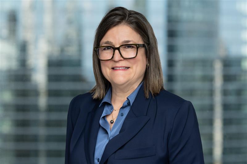 Minsky, McCormick & Hallagan, P.C. Excited to Expand its Federal Litigation Practice by Adding Robert Carpenter & Patricia Capt Woman with shoulder-length brown hair wearing glasses, a blue blouse, and a navy blazer, standing in front of a blurred office window background.